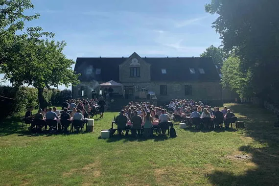 Stort selskab til picnic på græsplænen foran en gammel gård