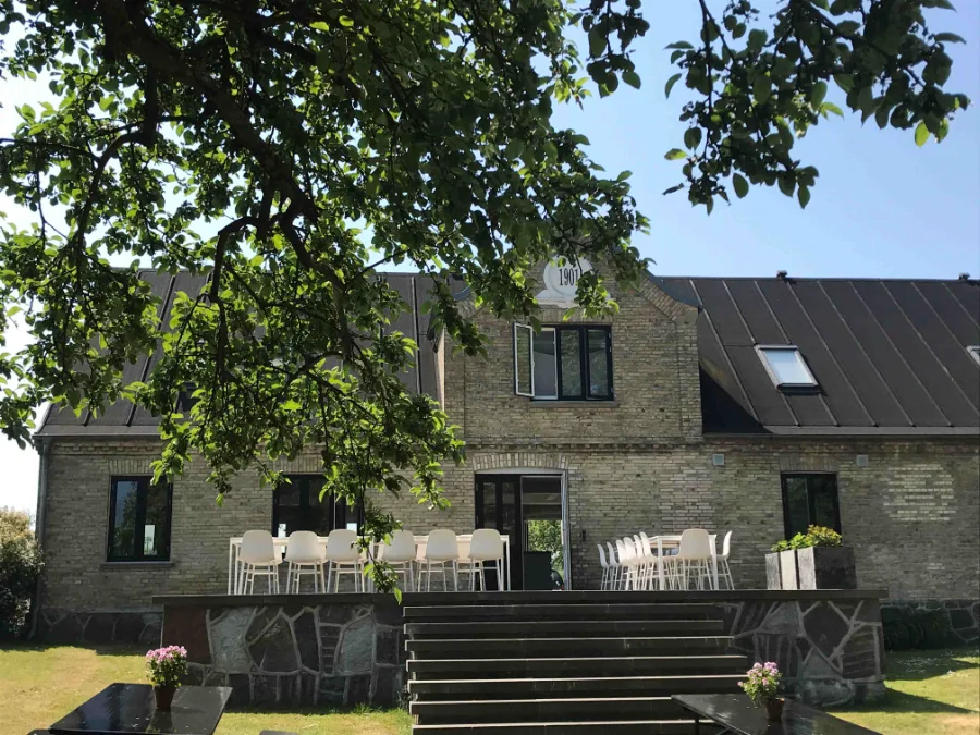 Gammelt stenhus med terrasse og store træer på Samsø